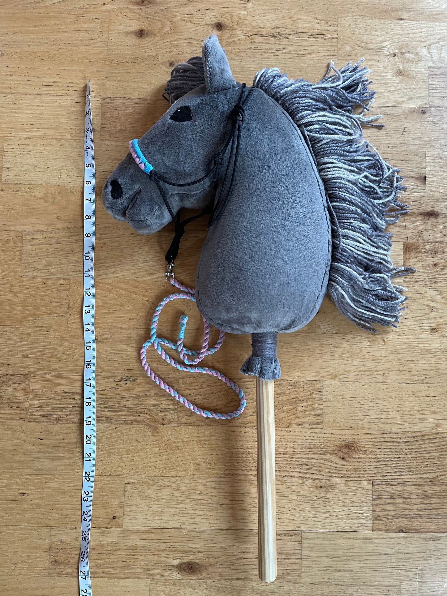 Gray hobby horse toy on a wooden floor with a measuring tape for scale.