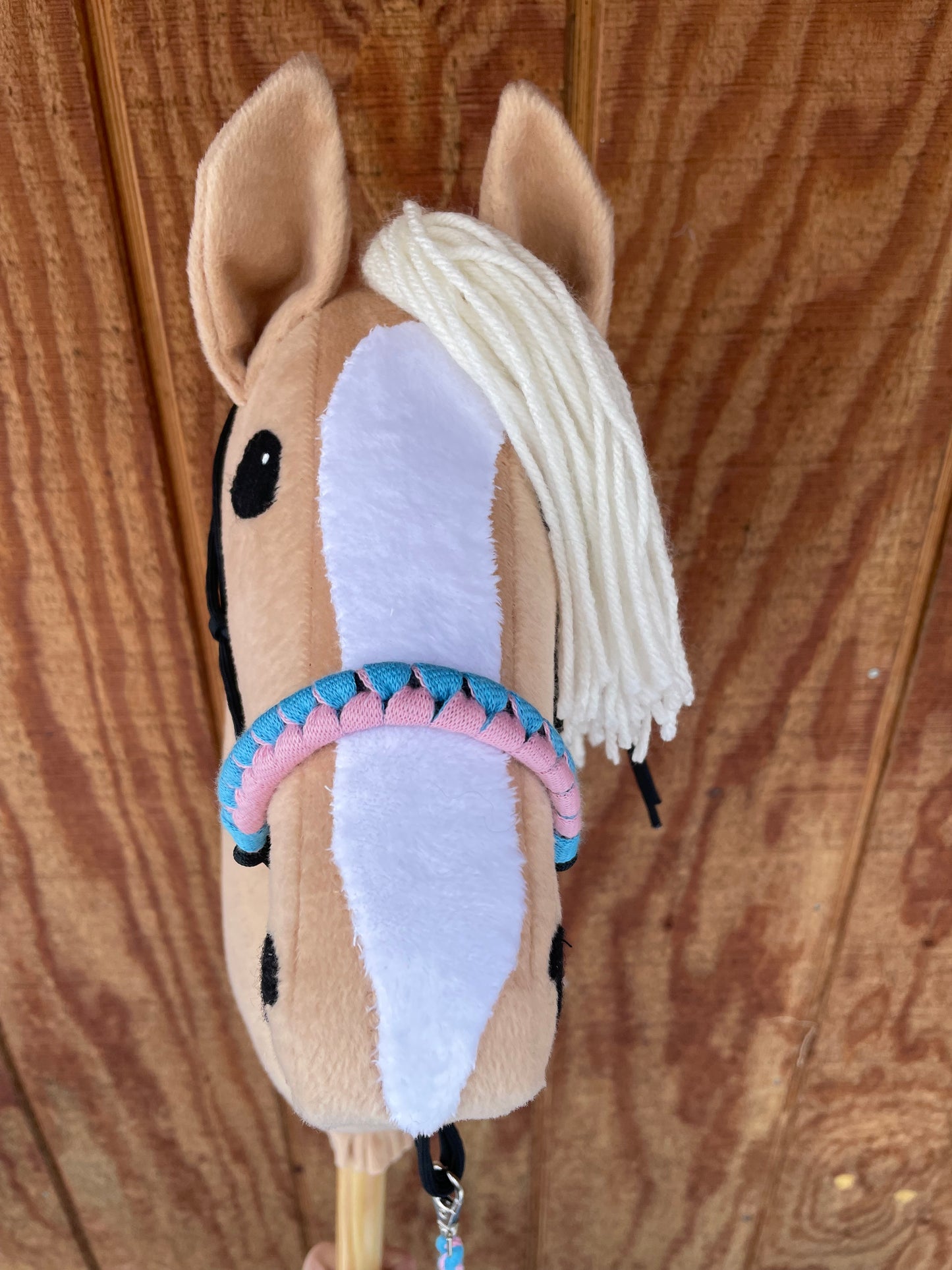 Beige hobby horse with a pink and blue halter on a wooden surface