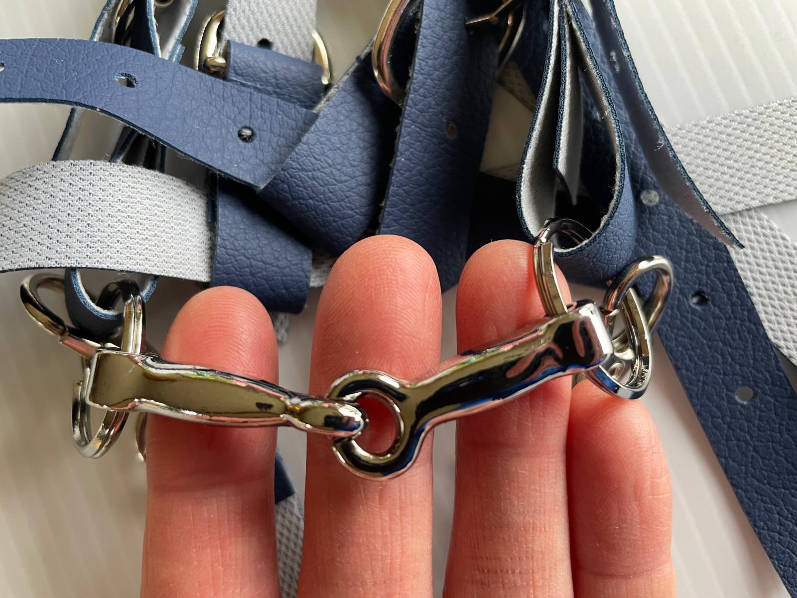 Metal horse bridle bit held between fingers with blue and gray straps in the background