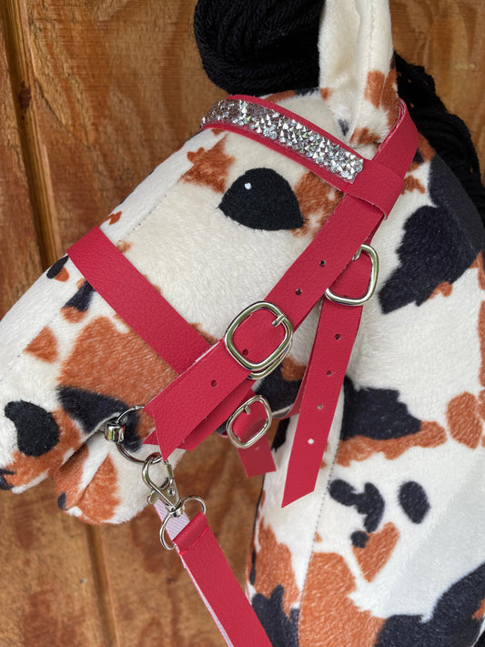 Pinto hobby horse wearing a red english bridle with silver bling on the browband. Wooden background.