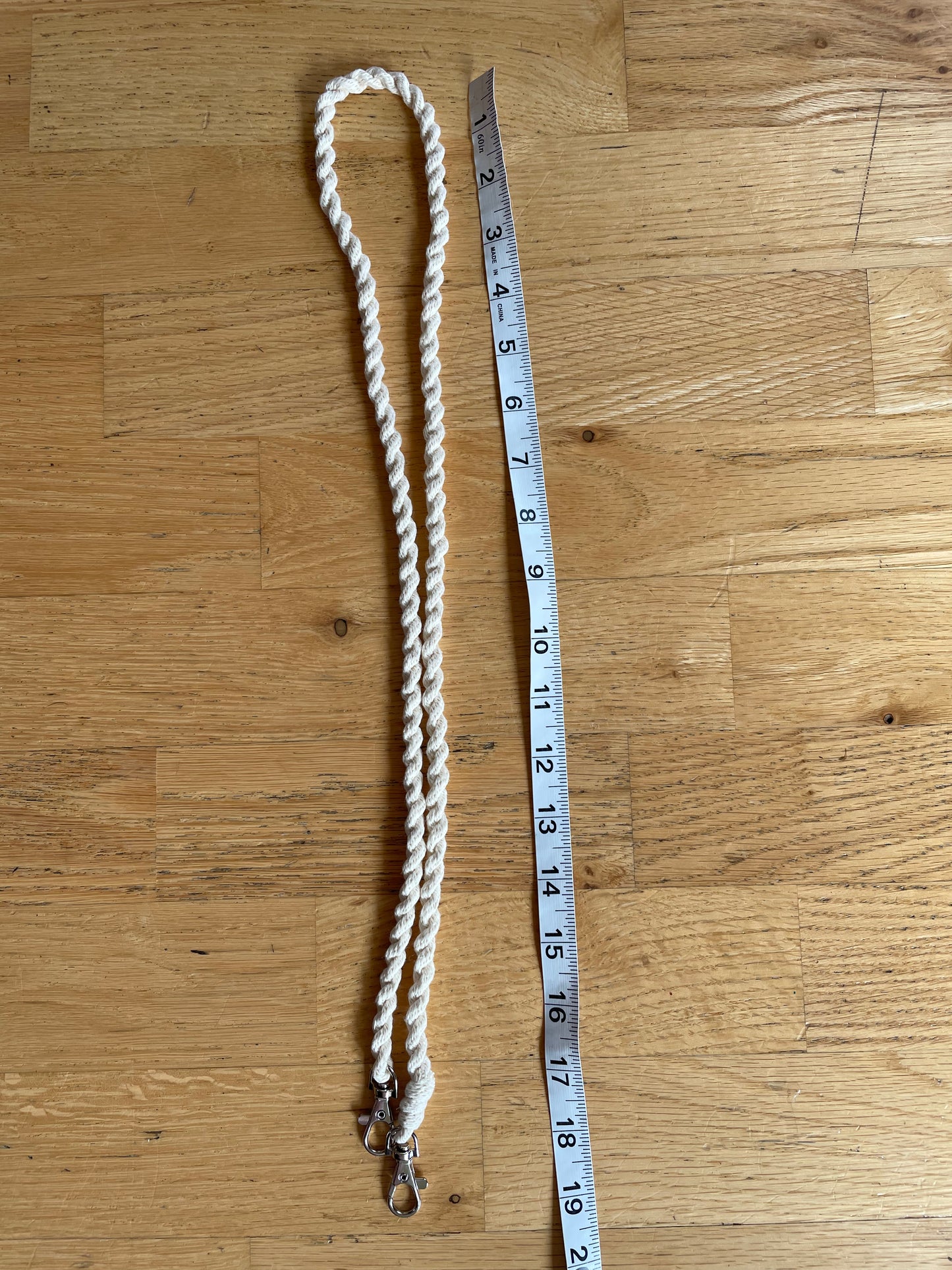 A cream-colored twisted hobby horse reins with metal clasps, shown next to a measuring tape on a wooden floor.
