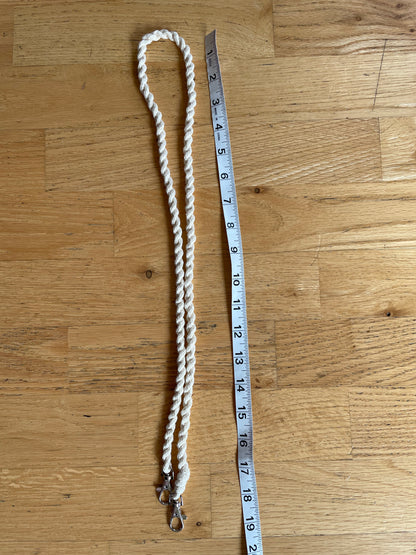 A cream-colored twisted hobby horse reins with metal clasps, shown next to a measuring tape on a wooden floor.