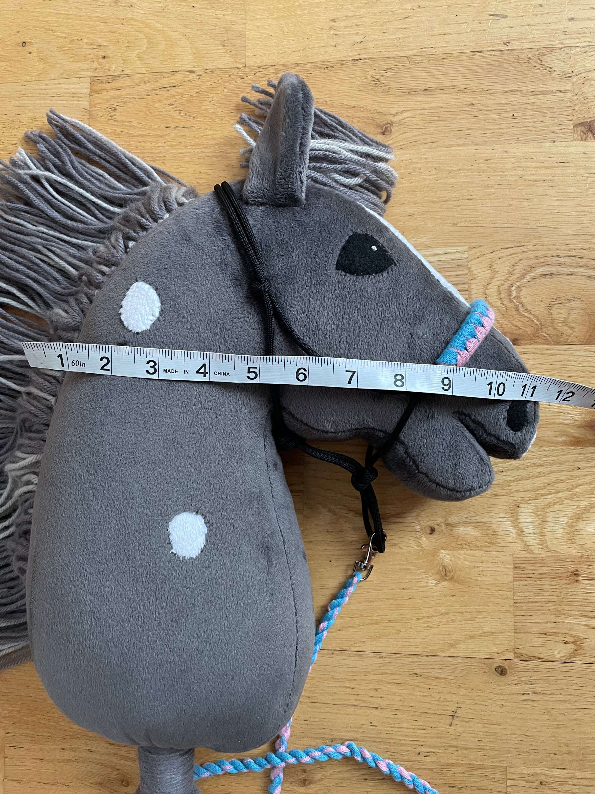 Hobby Horse dark gray with halter. Showing width of the horse with measuring tape. Wooden background.