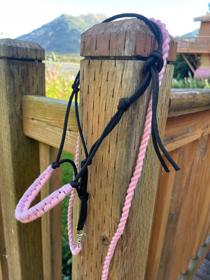 Black hobby horse rope halter with pink and purple on wooden surface outside.