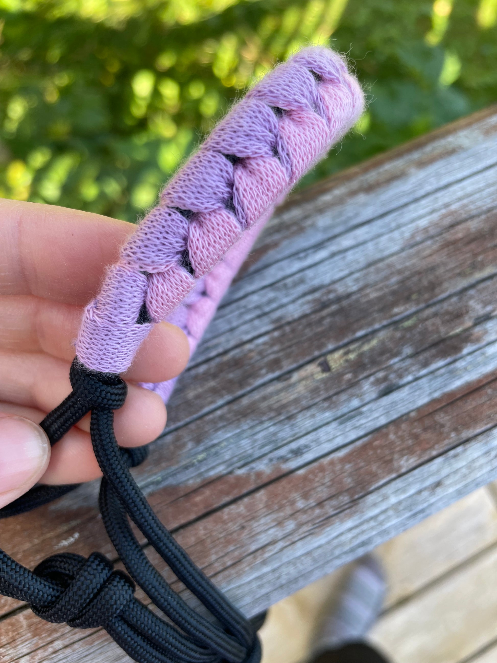 Hand holding a hobby horse rope halter against a wooden background. Showing pink and purple close up.