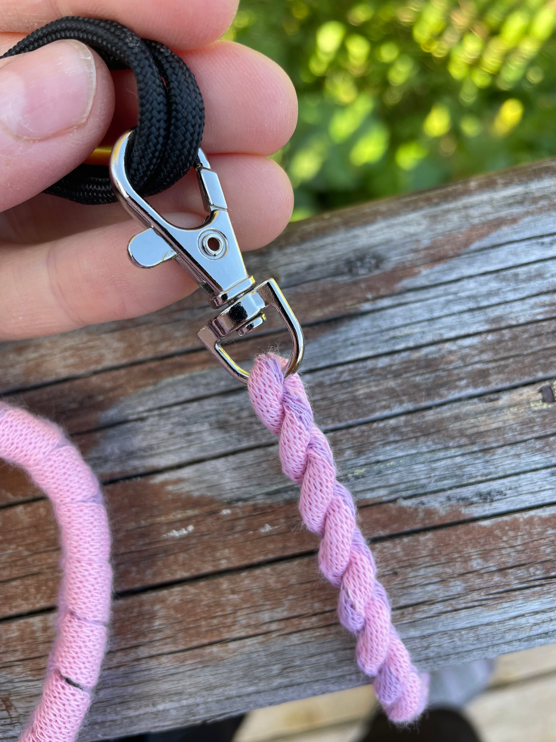 Pink and purple hobby horse lead rope with a metal clip held by a hand against a wooden background.