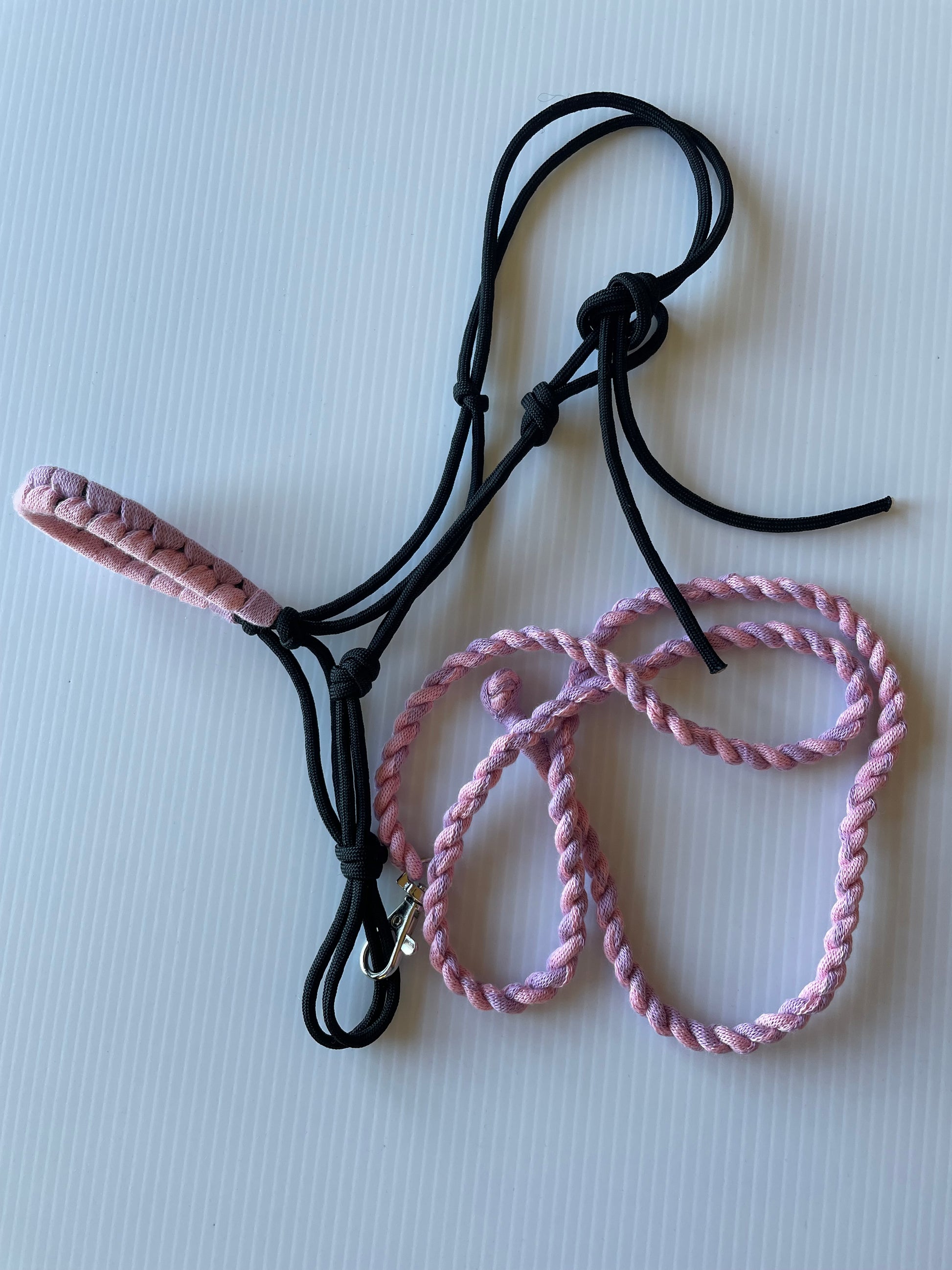 Black hobby horse rope halter with pink and purple on white surface.