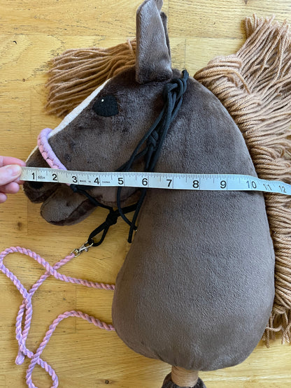Brown plush hobby horse toy with a measuring tape on a wooden floor. Horse has a rope halter on.