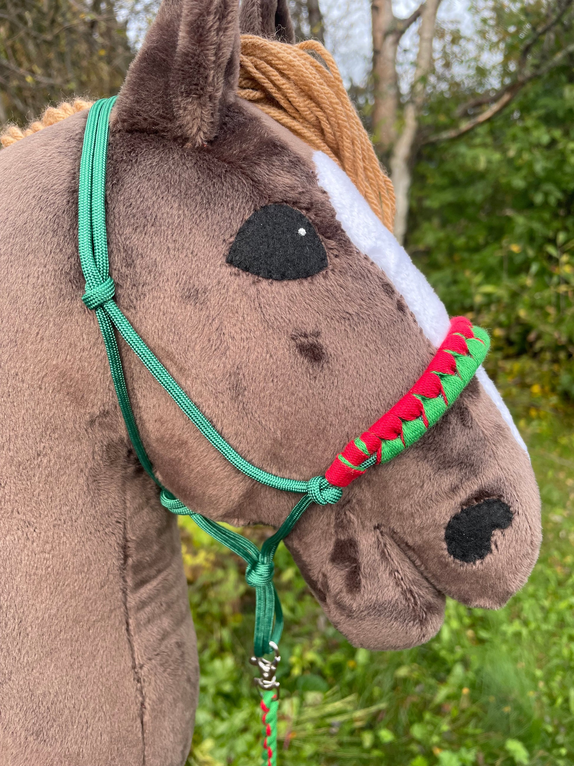 Close-up of a stuffed hobby horse with a green and red halter against a natural background.