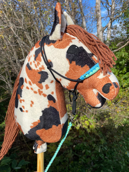 Hobby horse cow pattern pinto wearing a halter against a natural background.