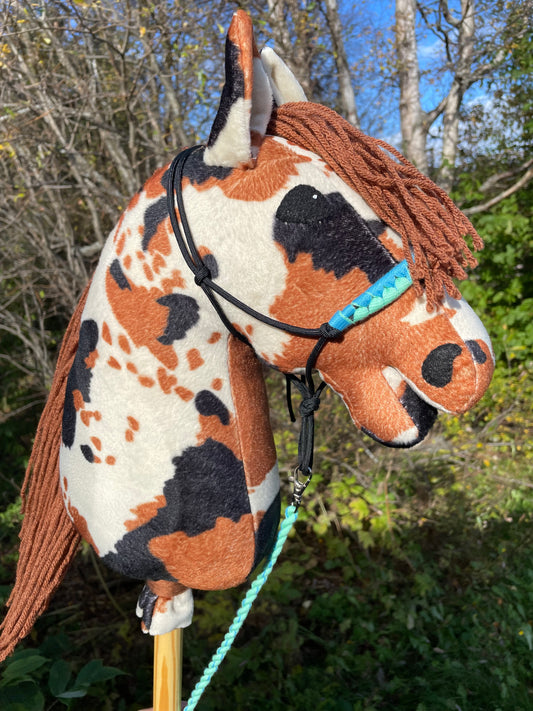 Hobby horse cow pattern pinto wearing a halter against a natural background.