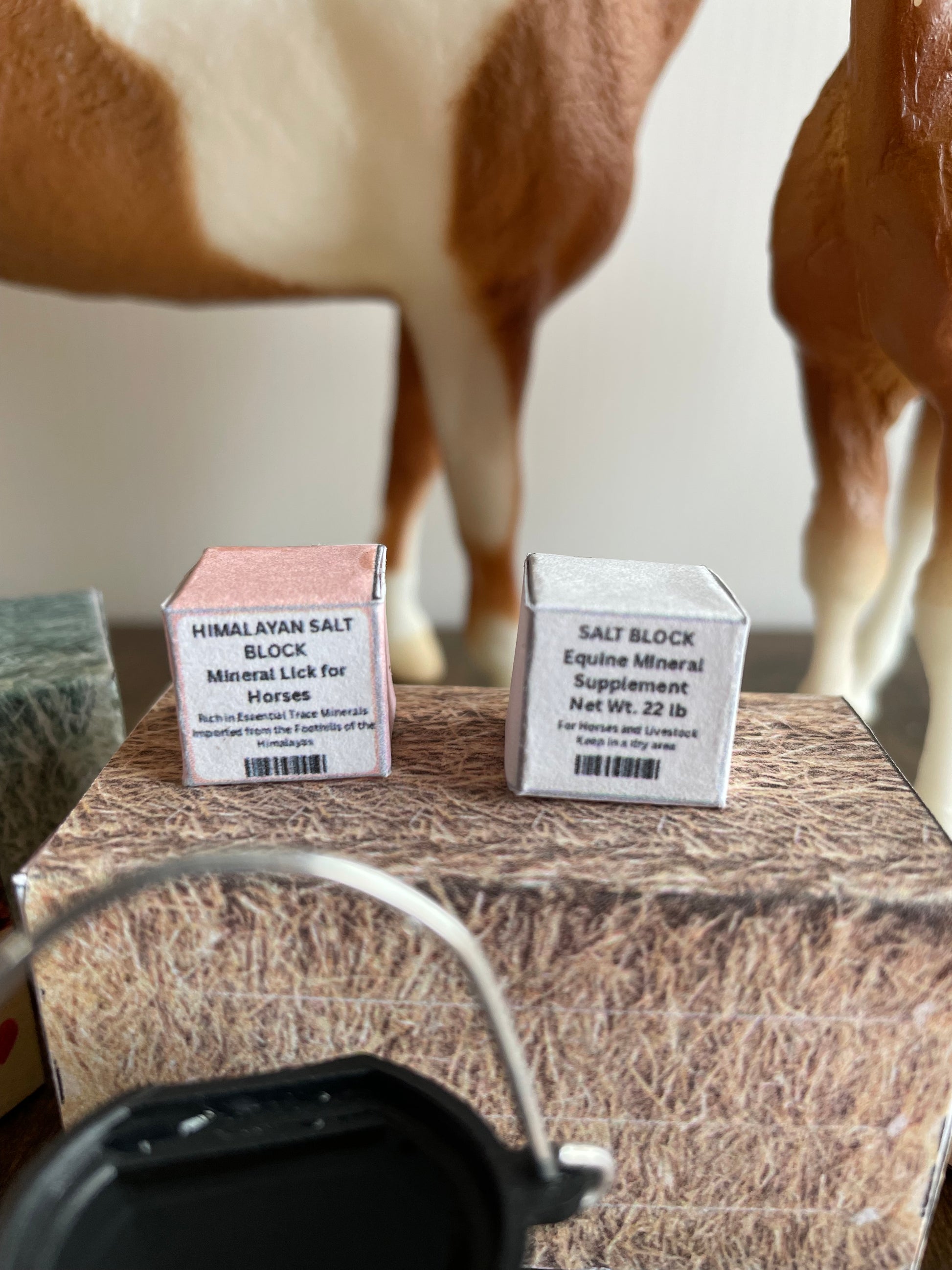 Two small miniature salt boxes on a wooden surface with a blurred background.