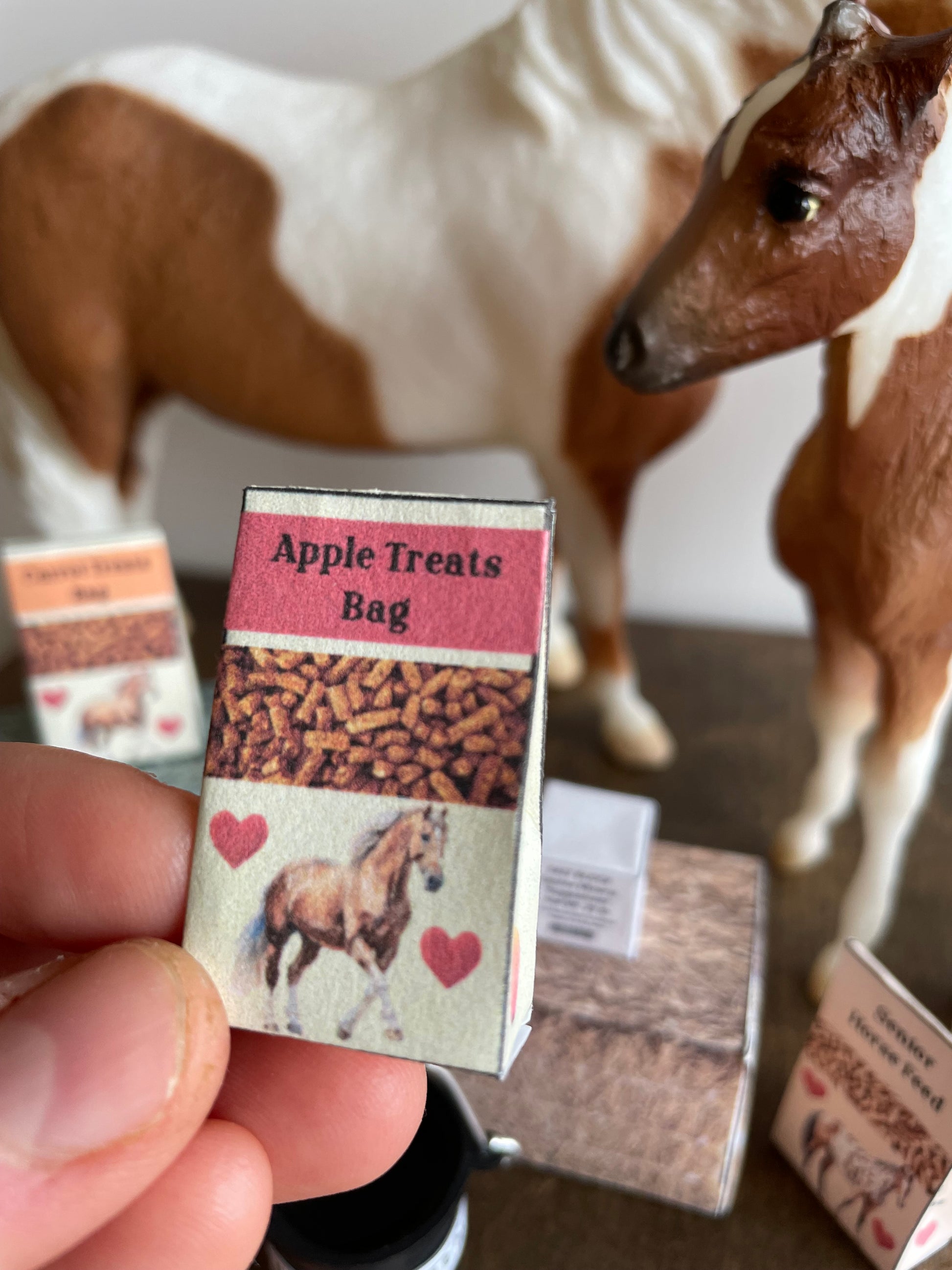 Miniature 'Apple Treats Bag' held by a hand, with a horse in the background.