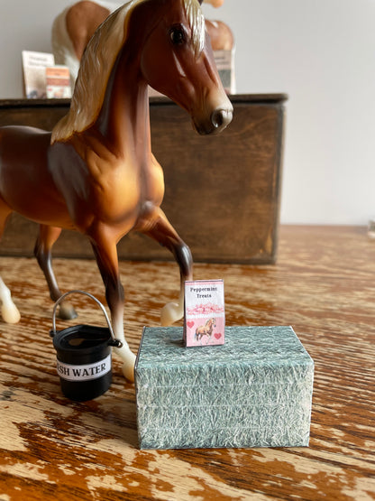 A horse and miniature hay bale and supplies on a wooden surface