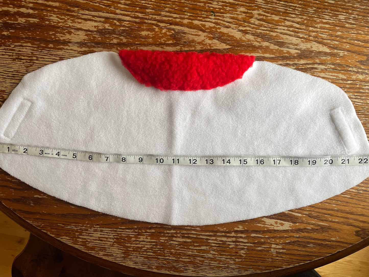White hobby horse with a red padding on a wooden surface, measured by a tape measure.