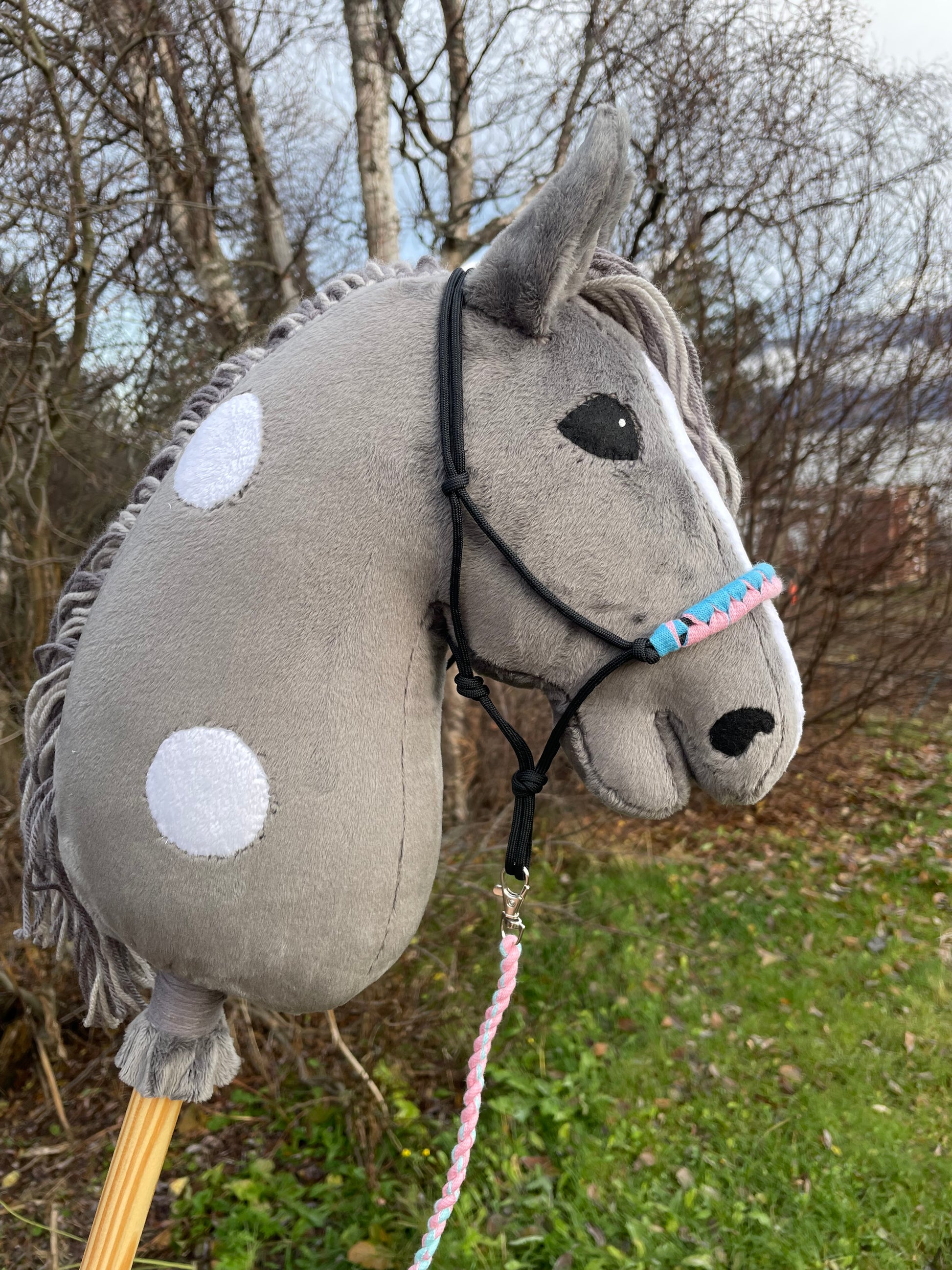 Plush toy gray hobby horse with white dots dots on a stick against a natural background