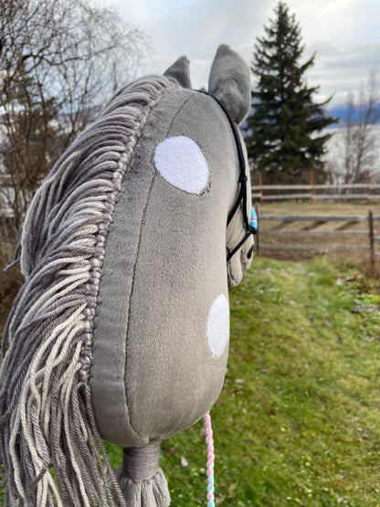 Plush toy gray hobby horse with white dots dots on a stick against a natural background, looking away.