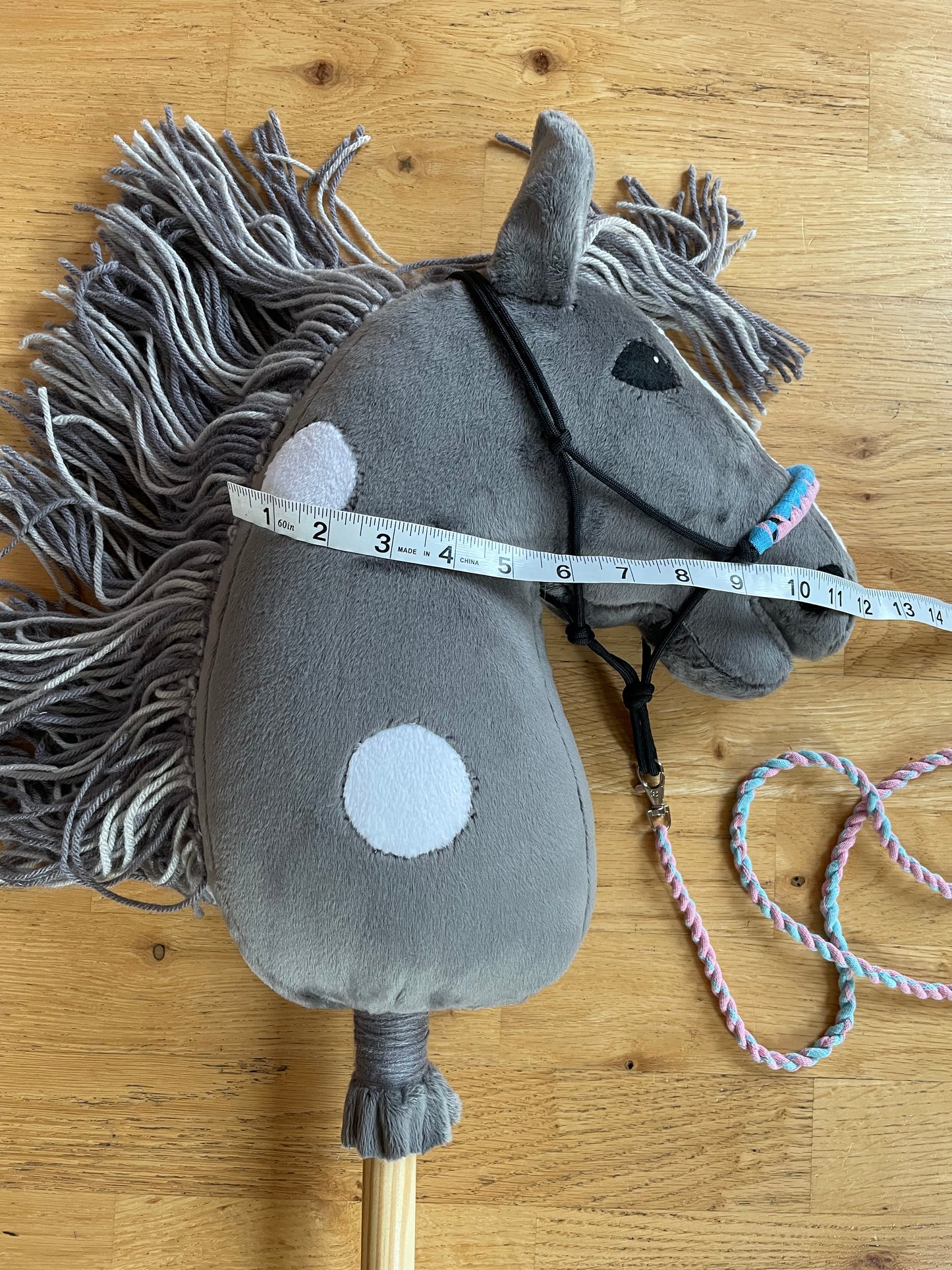 Gray plush hobby horse toy with a measuring tape on a wooden surface