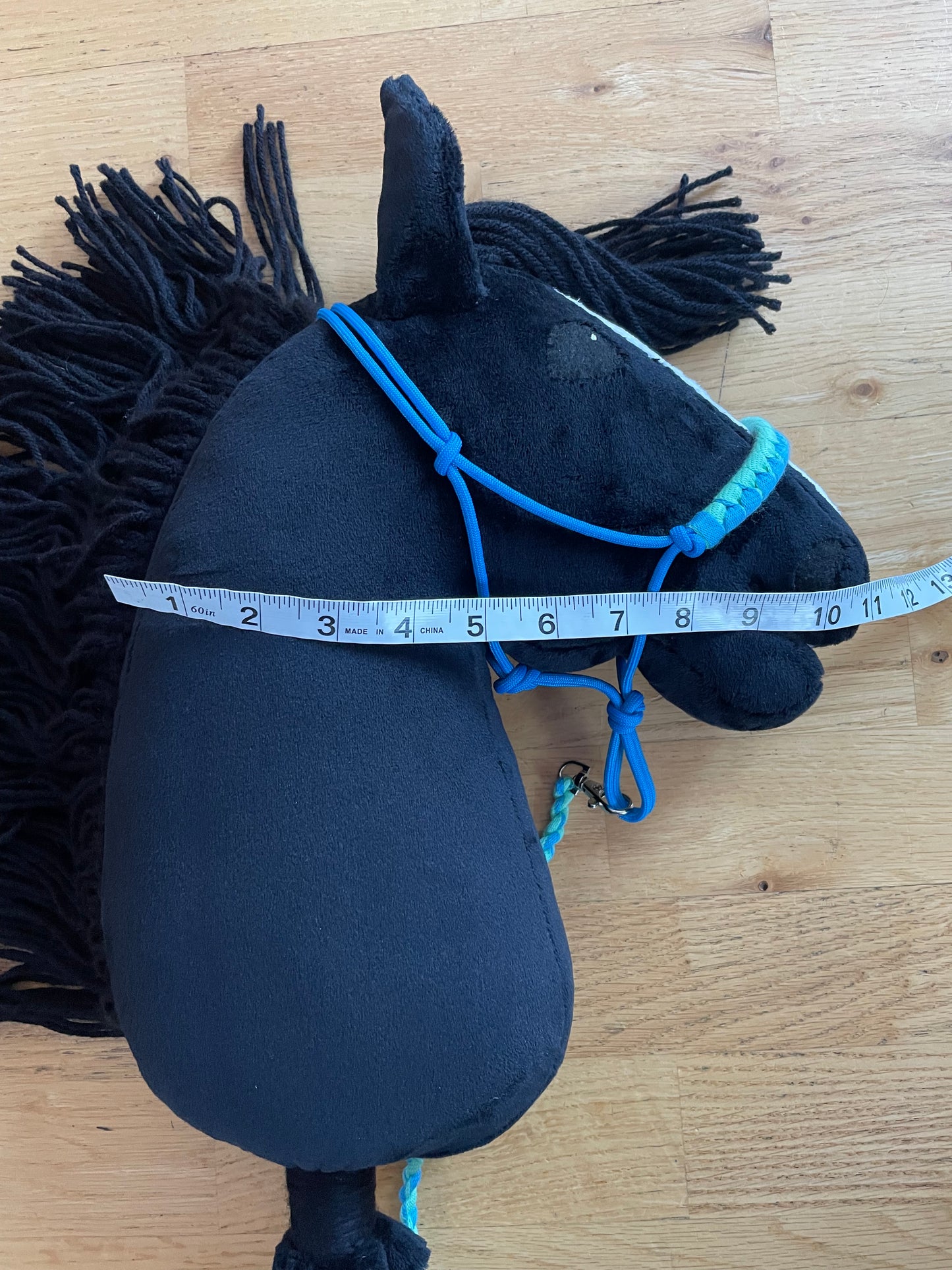 Black hobby horse with blue halter on  on a wooden floor, measured with a tape measure.