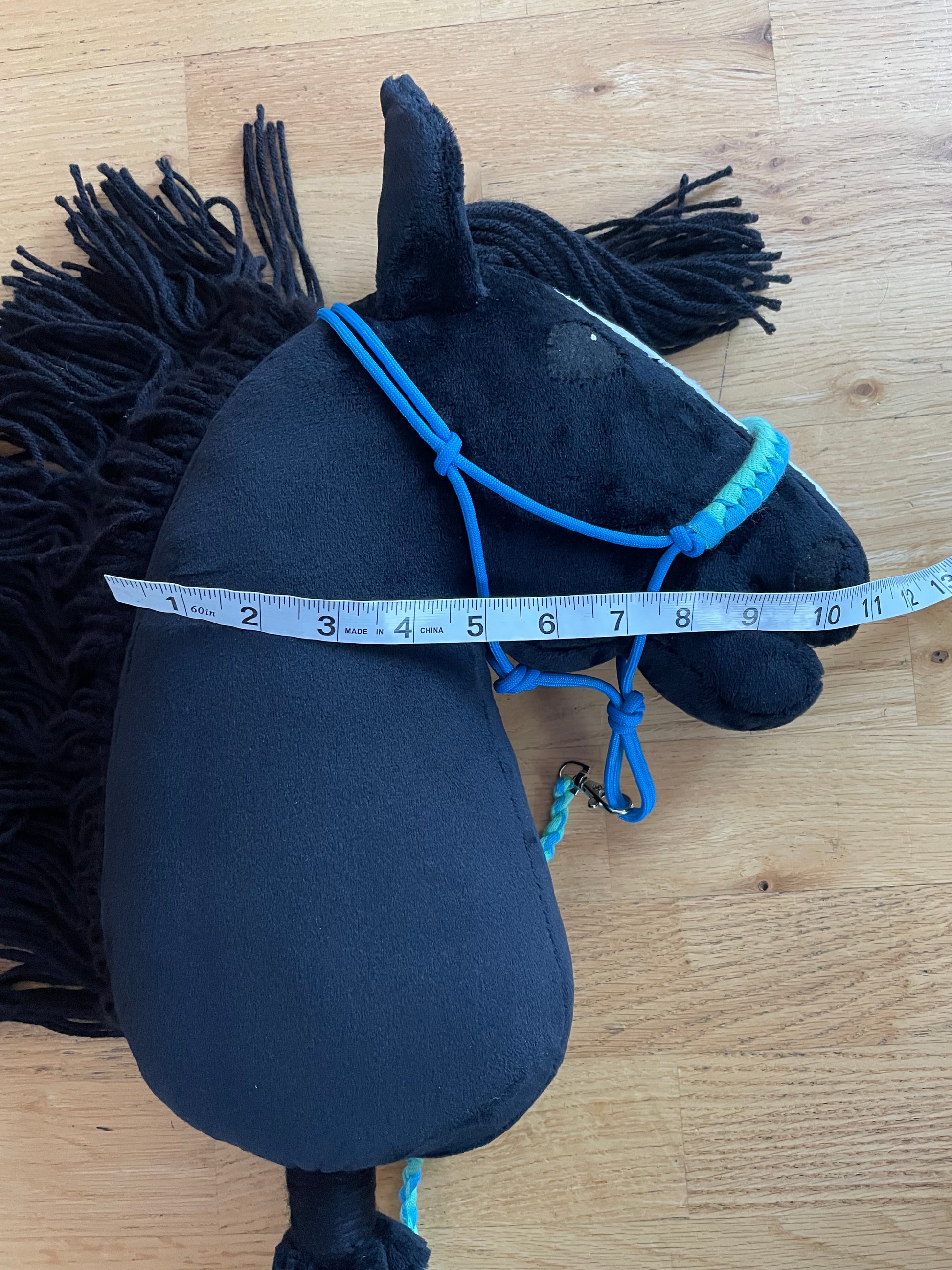 Black hobby horse with blue halter on  on a wooden floor, measured with a tape measure.