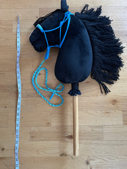 Black hobby horse with blue halter on  on a wooden floor, measured with a tape measure.