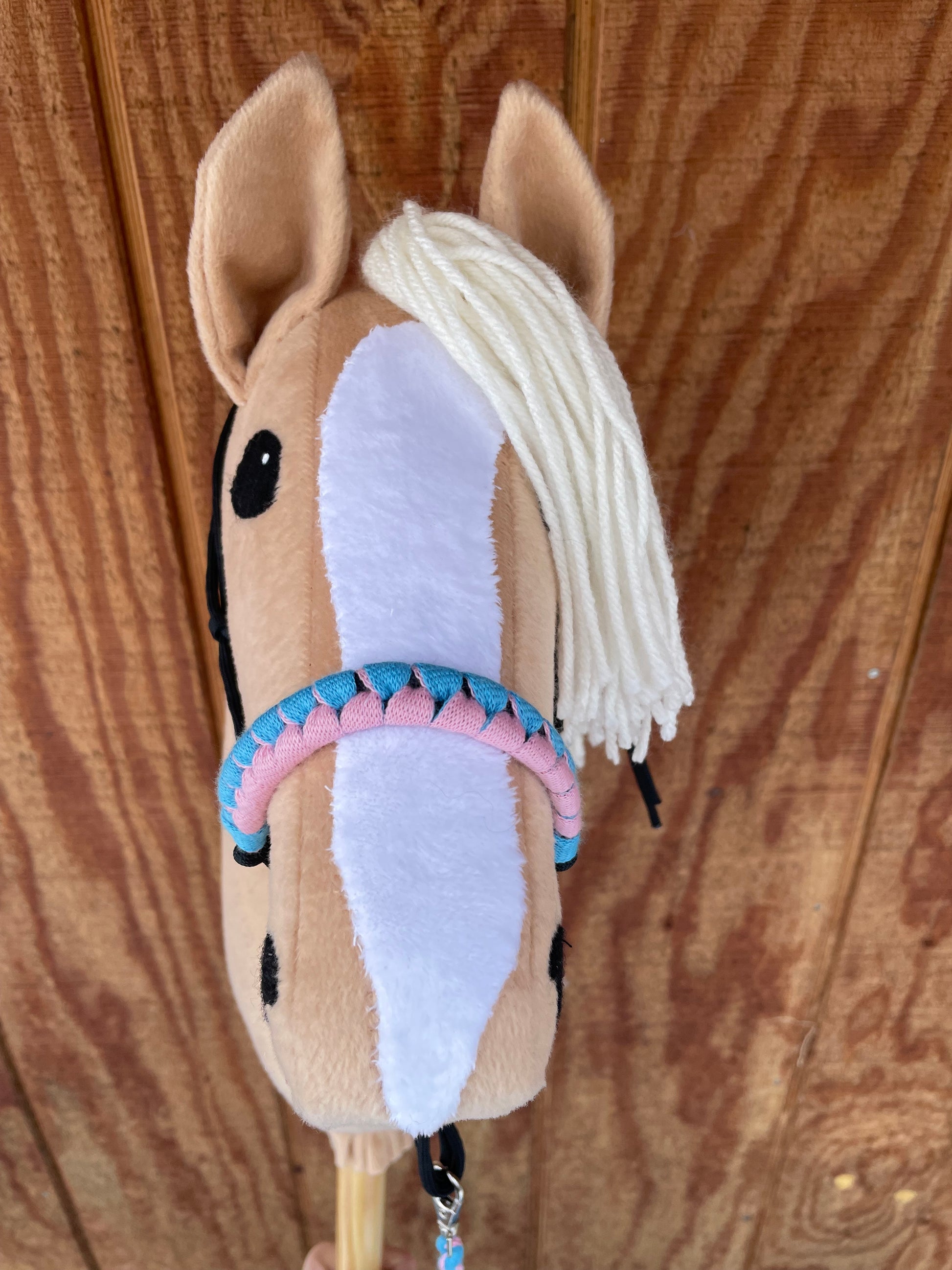 Beige hobby horse with a pink and blue halter on a wooden surface