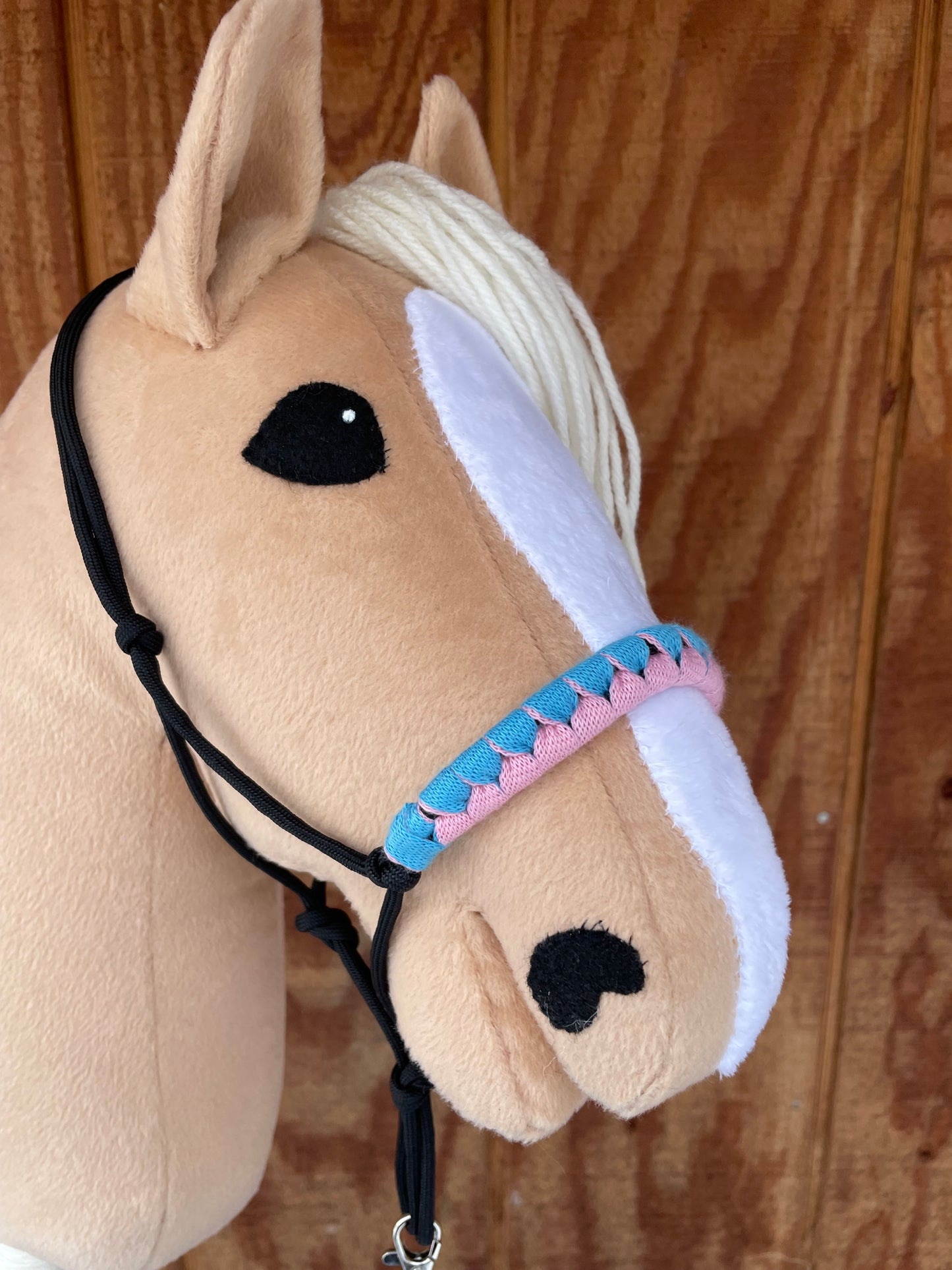 Close-up of a plush toy hobby horse with a pink and blue bridle on a wooden surface