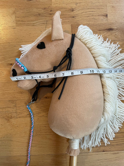 Beige plush hobby horse toy with a measuring tape on a wooden floor
