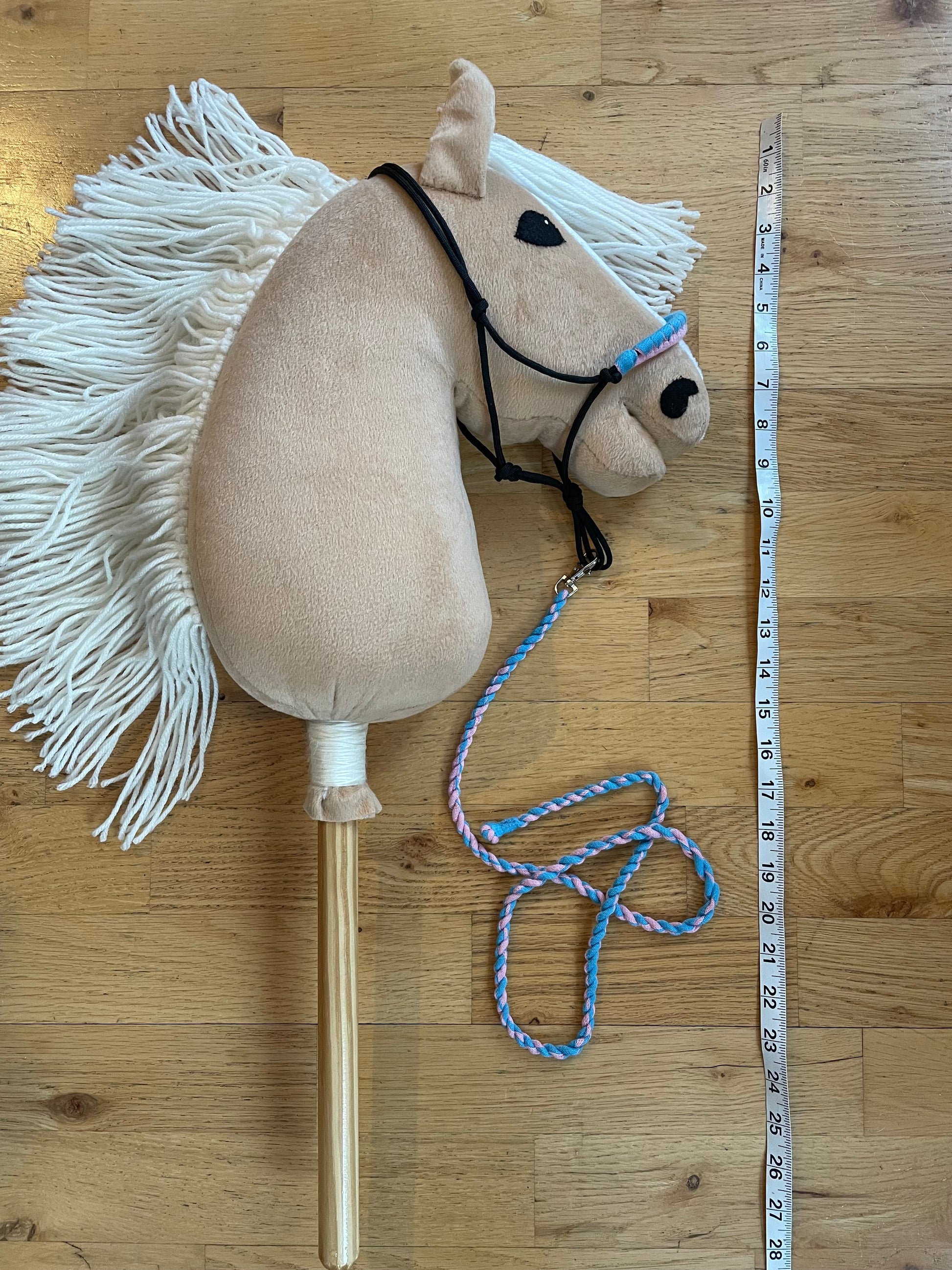 Plush hobby horse toy with a measuring tape for scale on a wooden floor