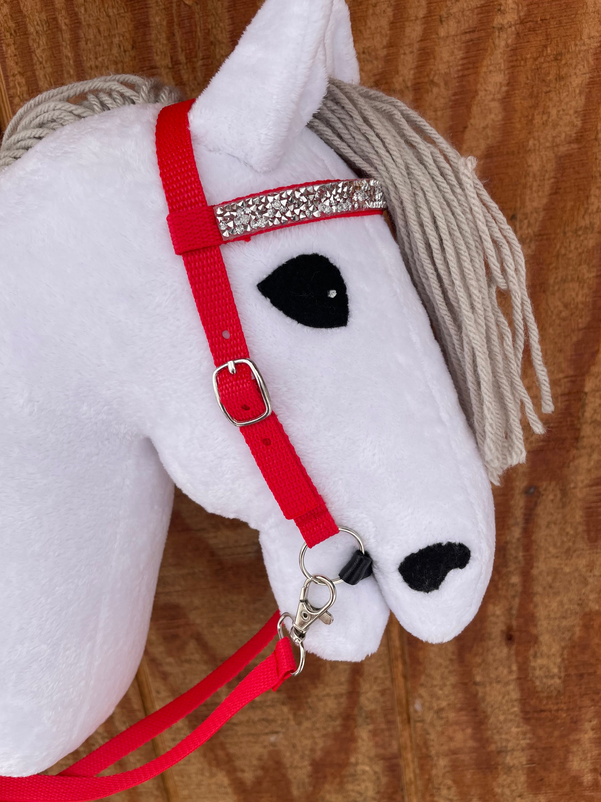 White hobby horse toy with a red bridle on a wooden surface