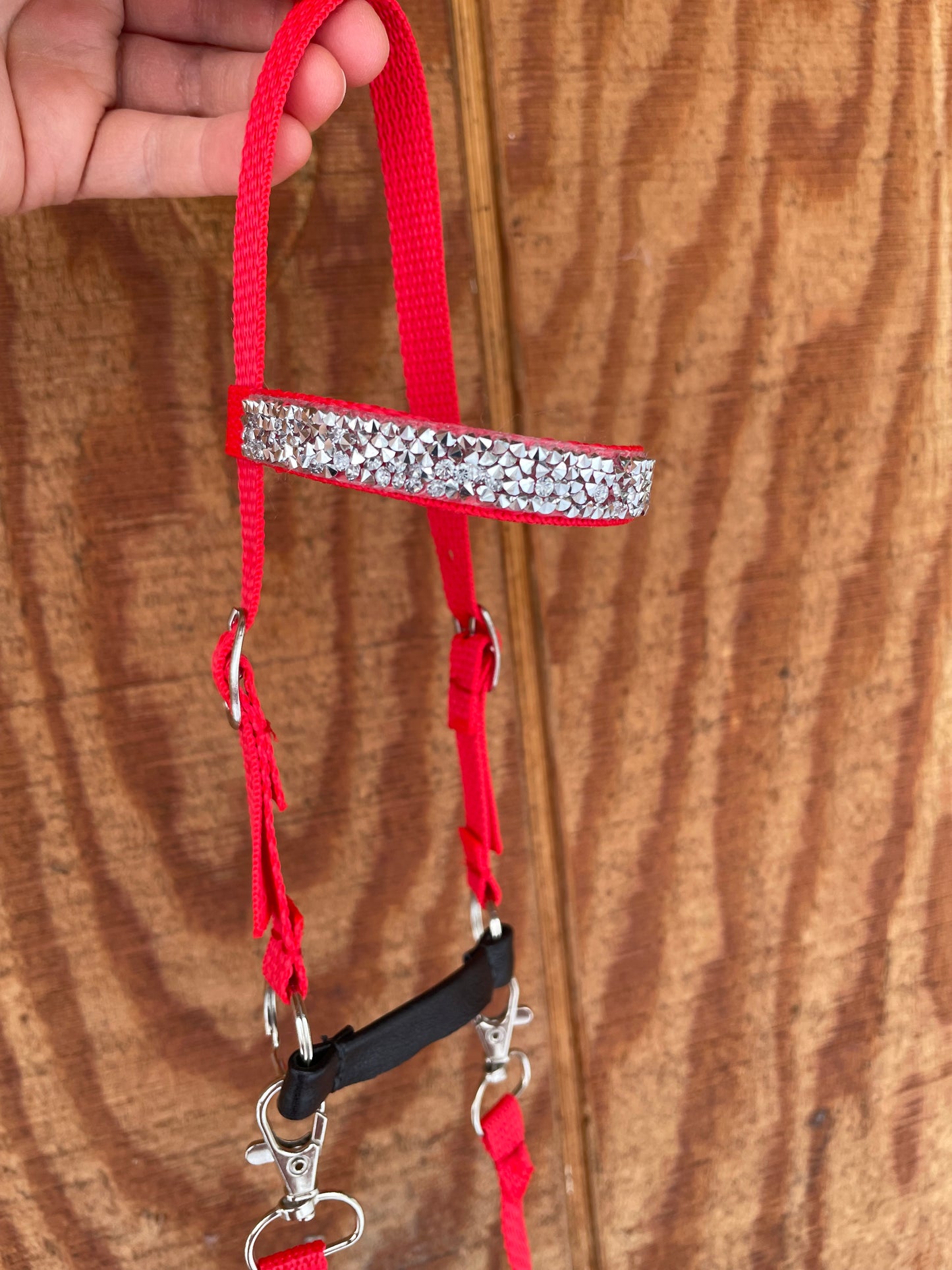 Red hobby horse bridle with rhinestone trim held by a hand on a wooden surface