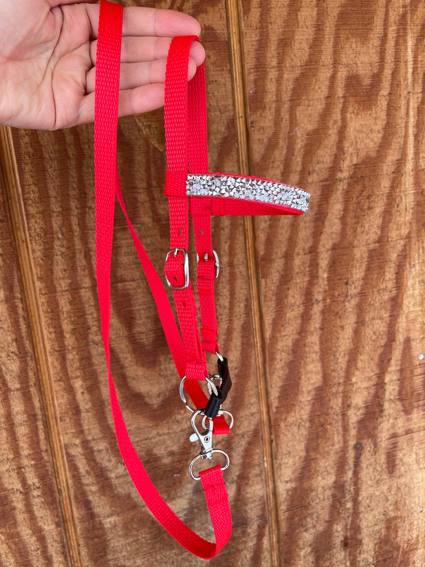 Red hobby horse bridle with a decorative silver bling held by a hand on a wooden surface