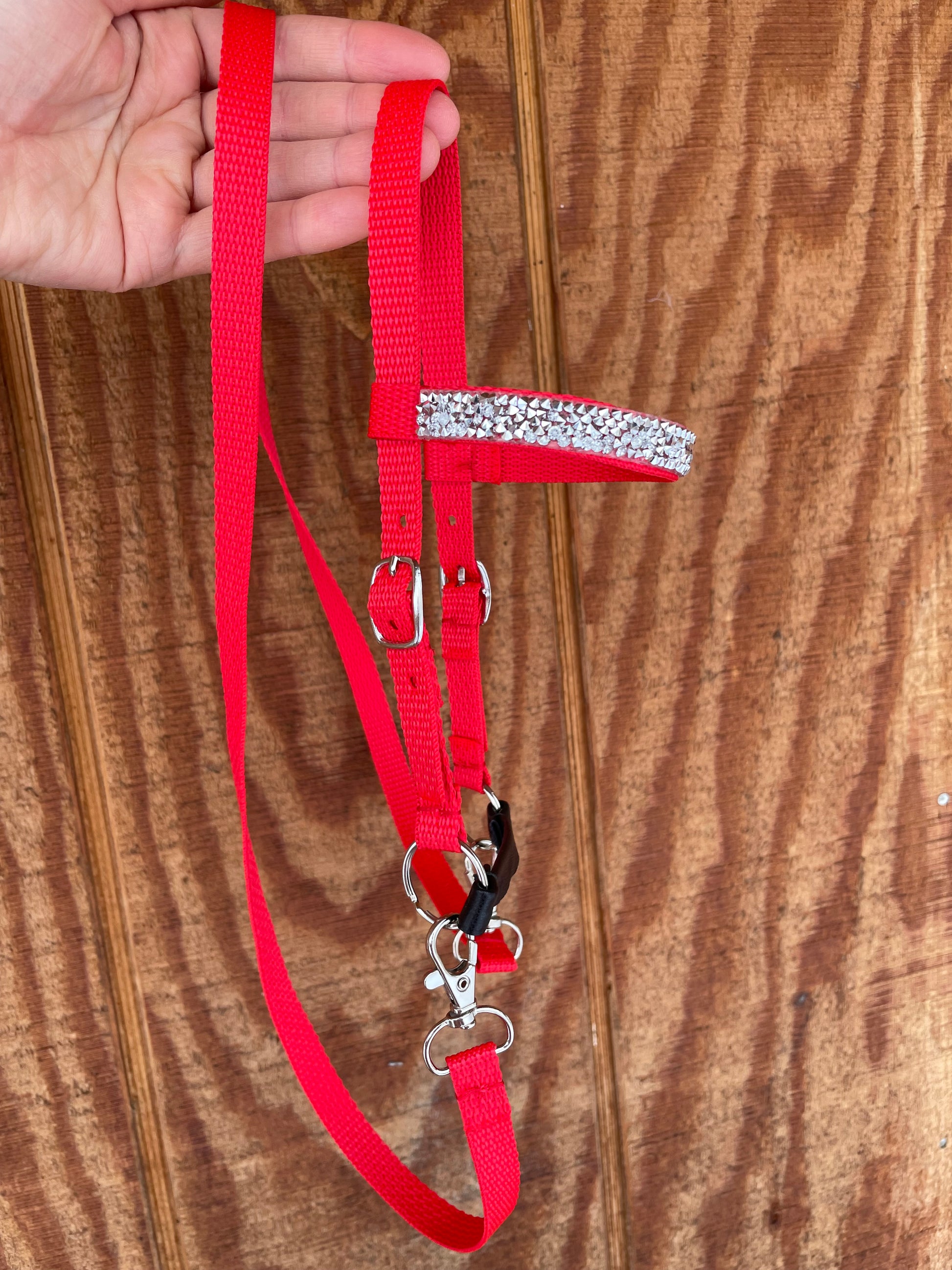 Red hobby horse bridle with a decorative silver bling held by a hand on a wooden surface
