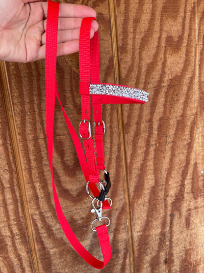 Red hobby horse bridle with a decorative silver bling held by a hand on a wooden surface