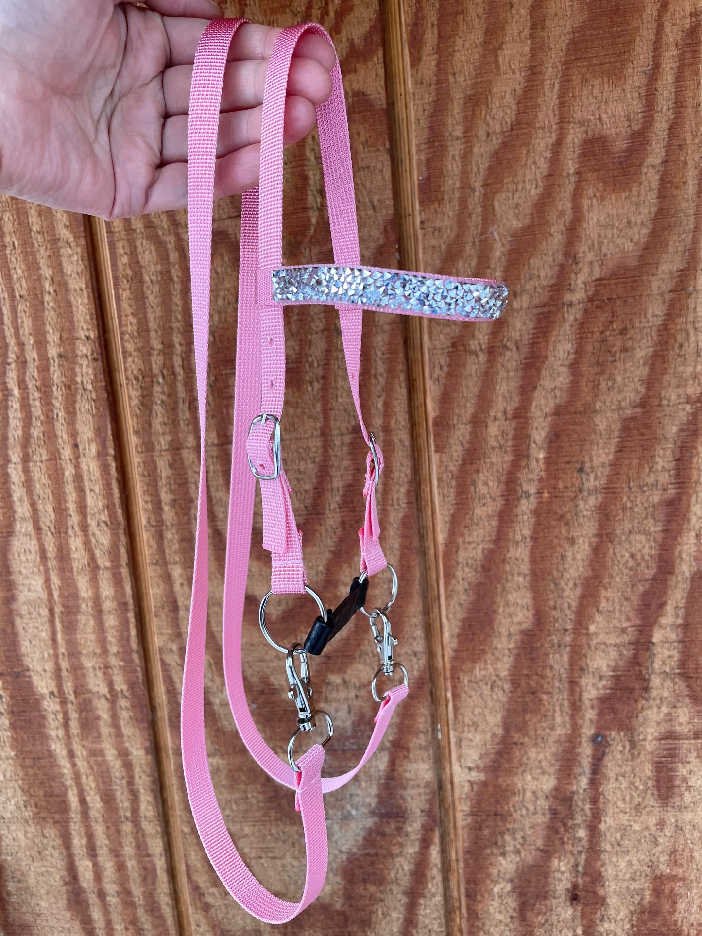 Pink hobby horse bridle with silver bling held by a hand on a wooden surface