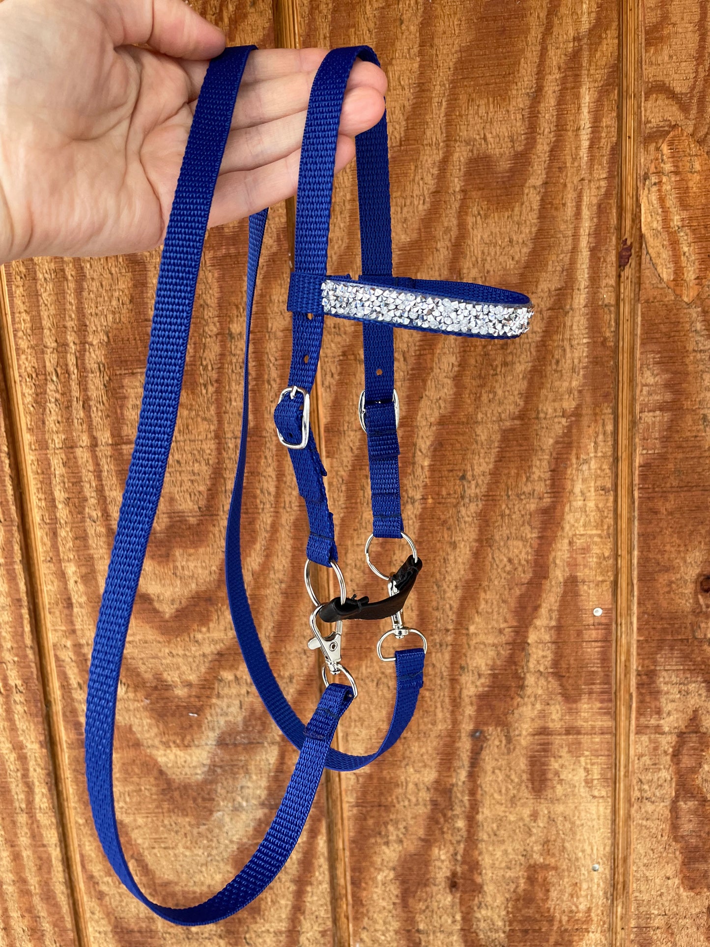 Blue hobby horse bridle with a silver bling held by a hand on a wooden surface