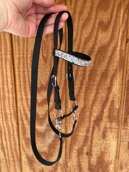 Black hobby horse bridle with silver bling held by a hand on a wooden surface