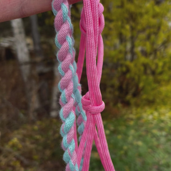 Hobby horse halter pink and lead rope on a green nature background. Halter is being held in a hand and it is hanging. 